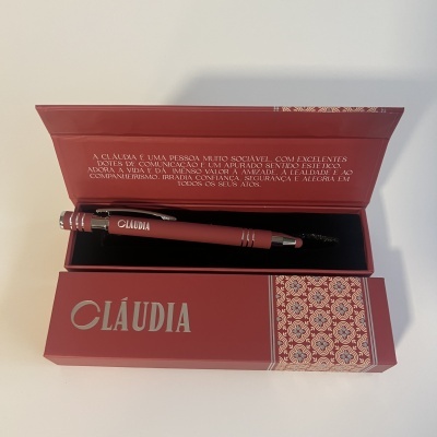 Caneta vermelha dentro de estojo vermelho com padrão geométrico e texto CLAÚDIA
