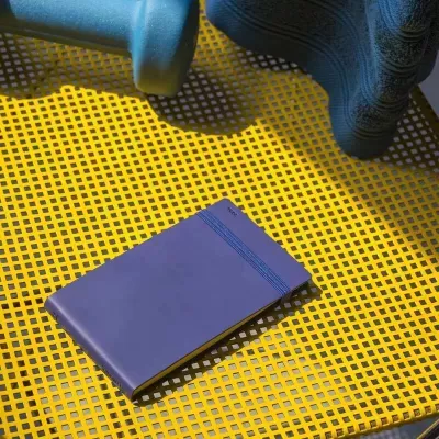 Caderno azul com elástico azul sobre rede plástica amarela