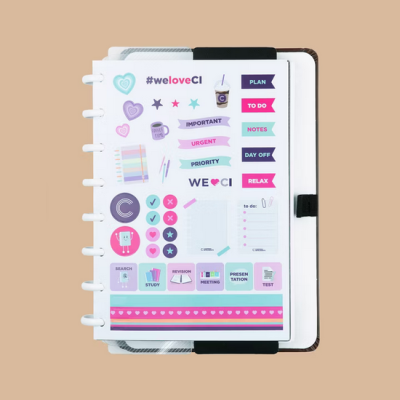 Folha com autocolantes coloridos para organização dentro de capa preta e branca sobre fundo bege