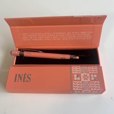 Caneta rosa dentro de caixa rosa com texto e padrões florais