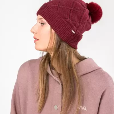 Mulher de perfil a usar gorro vermelho com pompom e camisola rosa claro com capuz