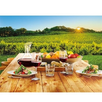 Mesa exterior com comida, vinho e frutas à frente de vinhas ao pôr-do-sol