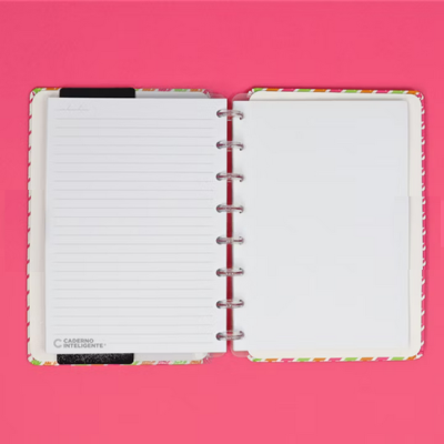 Caderno de argolas aberto com capa colorida e páginas brancas em fundo cor de rosa