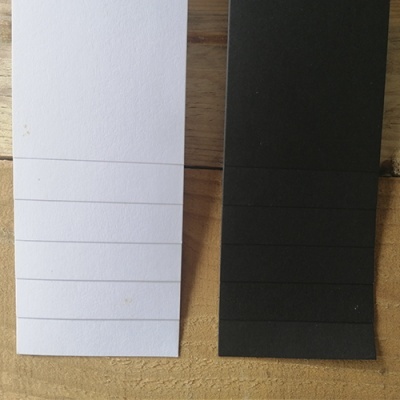 Peças de papel branco e preto com dobras horizontais sobre madeira clara