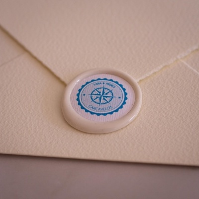 Envelope creme com selo de cera branca e etiqueta azul com bússola e texto