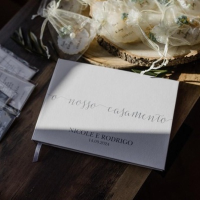 Livro de assinaturas de casamento branco com texto e pequenos saquinhos e pacotes sobre mesa de madeira