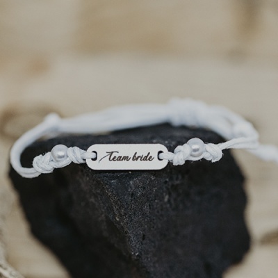 Pulseira branca com placa metálica com inscrição Team bride sobre pedra preta