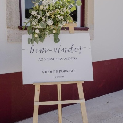 Placa de boas-vindas de casamento com flores em suporte de madeira junto a parede branca bordô