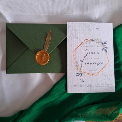 Convite de casamento com envelope verde escuro, selo de cera dourado e pena, e cartão branco texturizado com texto de casamento