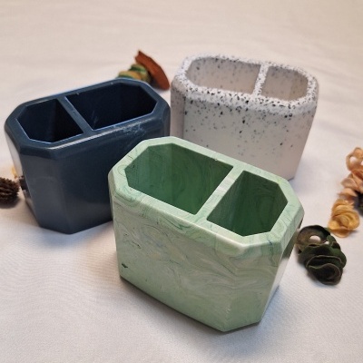 Três organizadores hexagonais para secretária em azul escuro, branco com manchas cinzentas e verde marmoreado, em tela branca com objetos naturais ao redor