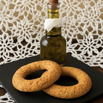 Duas broas redondas com garrafa pequena de vidro e tampa de cortiça em placa preta, fundo rendado branco