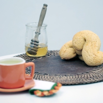 Biscoitos, jarra de mel com colher e chá em conjunto de cerâmica cor de laranja sobre mesa branca