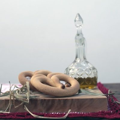 Biscoitos em forma de anel sobre suporte de madeira com tecidos bordados e jarro de vidro ao fundo