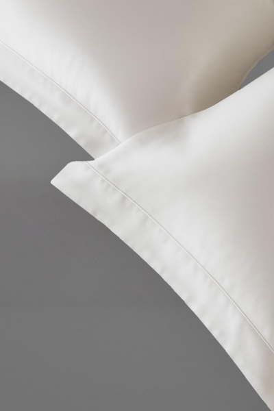 Almofadas brancas com costura dupla sobre roupa de cama cinza