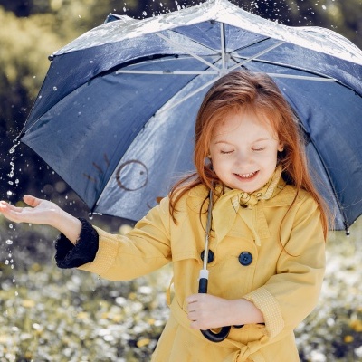 Menina com guarda-chuva azul e casaco amarelo na chuva ao ar livre