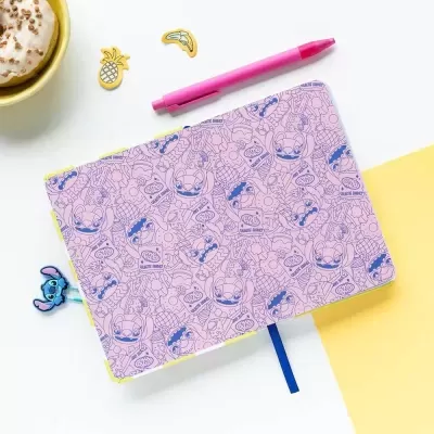 Caderno rosa com desenhos azuis, caneta rosa e autocolantes sobre mesa branca e amarela
