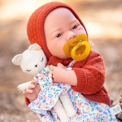 Boneca realista vestida com camisola vermelha e vestido floral segurando brinquedo de pano e chupeta amarela
