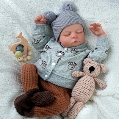 Bebé vestido com casaco cinzento de veados, calças castanhas de malha, gorro cinzento com pompons, deitado numa manta branca com brinquedos