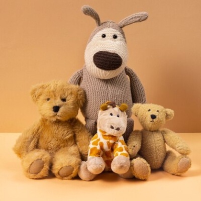 Quatro peluches de diferentes animais e cores sobre superfície e fundo bege.