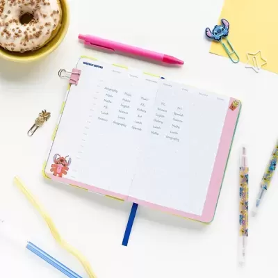 Caderno aberto com texto de treino de escrita e material de escritório colorido ao redor