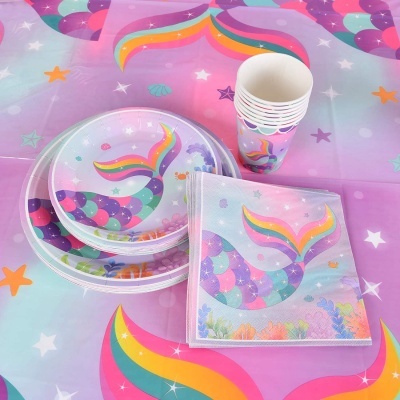 Conjunto de festa tema sereia com pratos, copos e guardanapos coloridos sobre toalha com padrão semelhante
