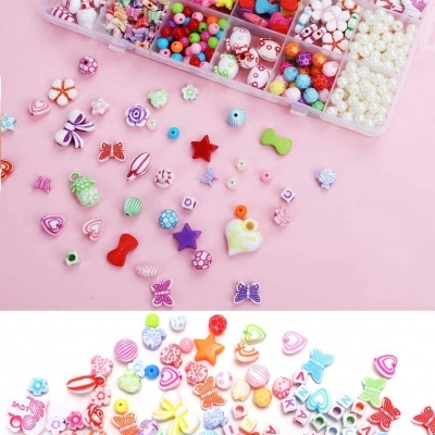 Contas coloridas para bijuteria organizadas em caixa plástica e espalhadas em superfícies rosa e branca