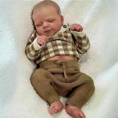 Boneco bebé realista com roupas de malha castanhas e bege sobre superfície branca macia