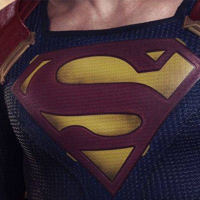 Fato de super-herói com símbolo 'S' vermelho e dourado no peito sobre fundo azul texturizado