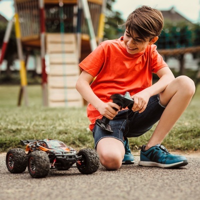 Rapaz com t-shirt laranja e ténis azuis a brincar com carro de controle remoto no parque