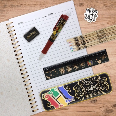 Conjunto escolar Harry Potter sobre caderno aberto numa mesa de madeira