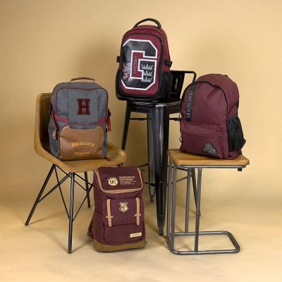 Mochilas em tons vinho e cinza sobre cadeiras e banco contra fundo bege