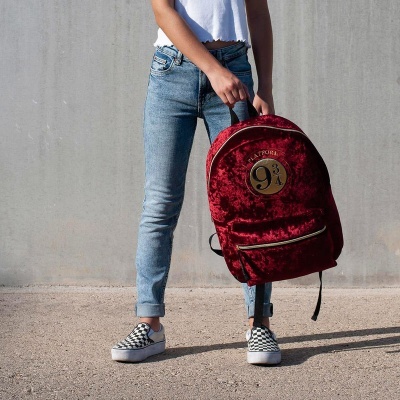 Mochila de veludo vermelha com estampado dourado 'Plataforma 9¾' segurada por pessoa com roupas casuais