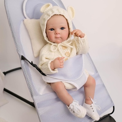 Boneca bebé realista vestida de malha creme num assento cinzento