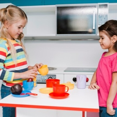 Duas crianças a brincar com cozinha em miniatura e acessórios coloridos.