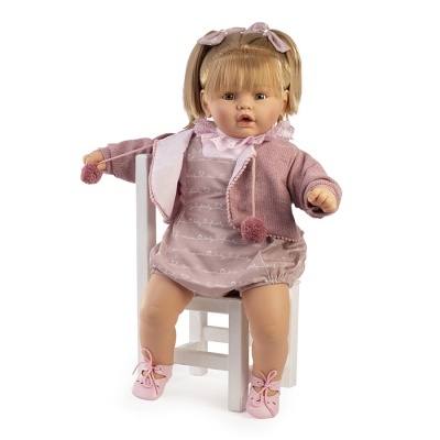 Boneca bebé com vestido e casaco rosa, sentada numa cadeira branca.