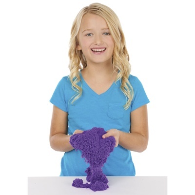 Menina loira com t-shirt azul segurando material texturizado roxo sobre mesa branca