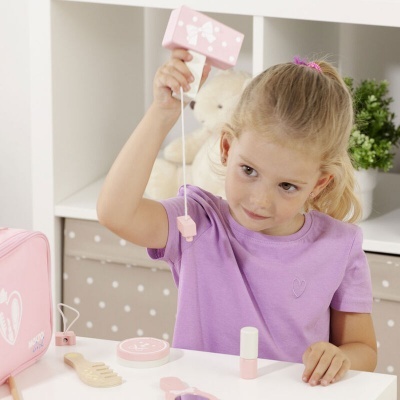 Menina loira a brincar com brinquedos de maquilhagem em tons rosa e lilás numa mesa branca