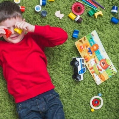 Criança a brincar num tapete verde com vários brinquedos coloridos ao redor