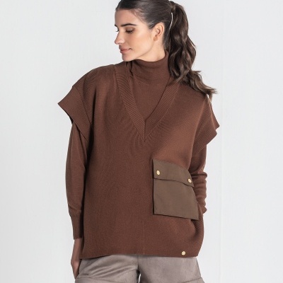 Mulher a usar colete castanho de malha com bolso frontal e calções cinzentos num fundo branco