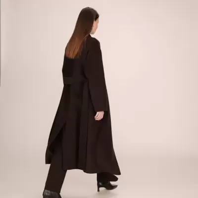 Mulher de costas com sobretudo comprido preto, calças pretas e botins de salto preto