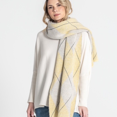 Mulher com echarpe amarela e cinza com padrão geométrico, camisola branca e calças de ganga