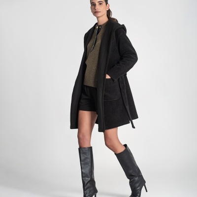 Mulher com casaco preto, camisola verde, calções pretos e botas pretas altas de salto