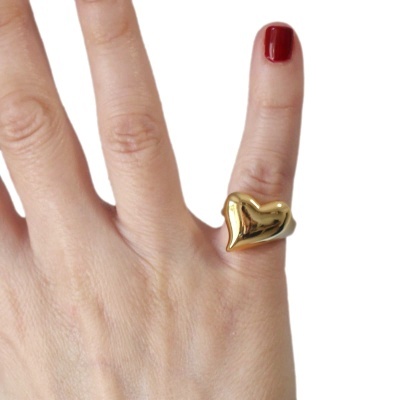 Anel dourado em forma de coração no dedo mindinho de uma mão com unha vermelha.