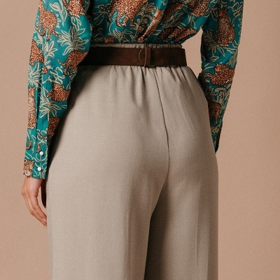 Parte traseira de mulher com camisa estampada e calças largas bege com cinto castanho