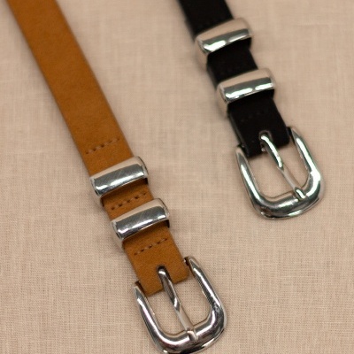 Dois cintos de couro, castanho claro e preto, com fivelas prateadas, sobre tecido bege
