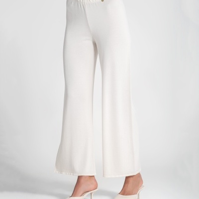 Calças brancas de tecido liso com cós elástico e sapatos brancos de salto médio.