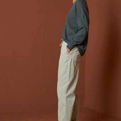 Mulher vestindo camisola verde, calças claras e sapatos castanhos em fundo castanho