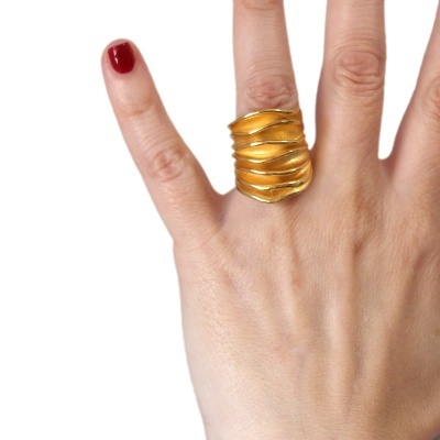 Anel dourado ondulado numa mão com unha vermelha