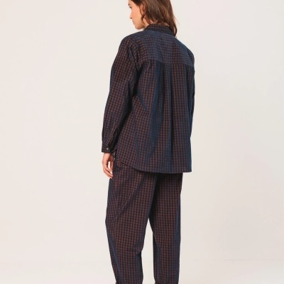 Mulher de costas vestindo pijama xadrez azul escuro com calças e camisa folgada, meias claras e sapatilhas desportivas