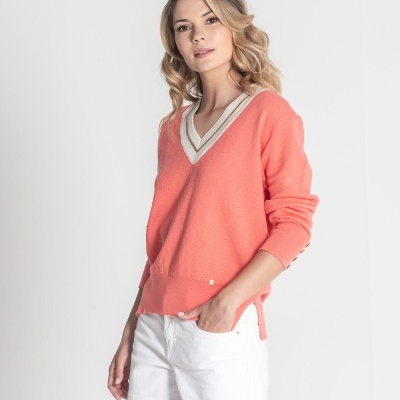 Mulher a usar camisola coral de gola em V com detalhes brancos e dourados e calções brancos.